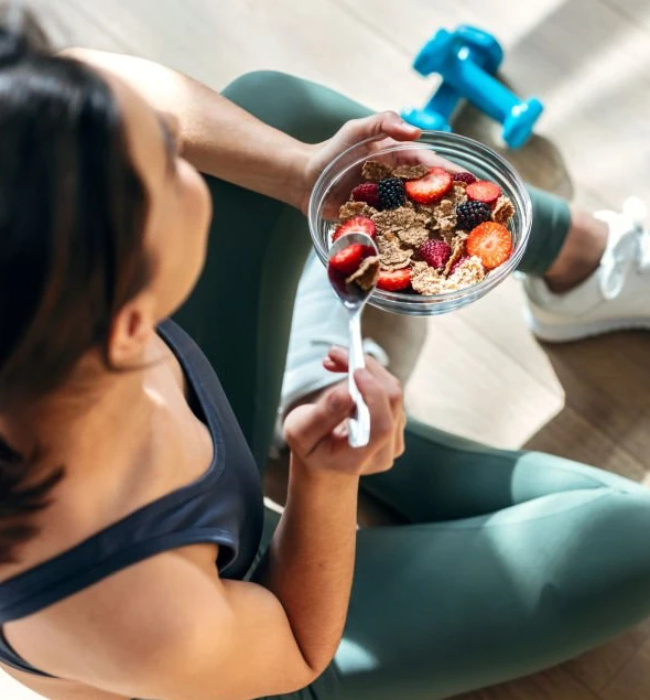 Une femme souriante en tenue de sport décontractée (legging et débardeur) boit une boisson protéinée et mange une banane après une séance de sport. après fais un coaching nutrition de Camille.